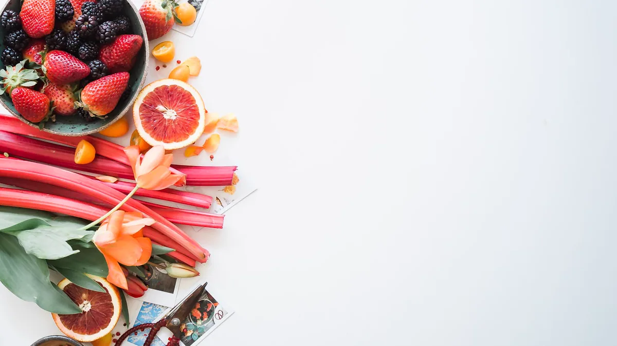 Berries, citrus fruit, and rhubarb arranged on a light surface