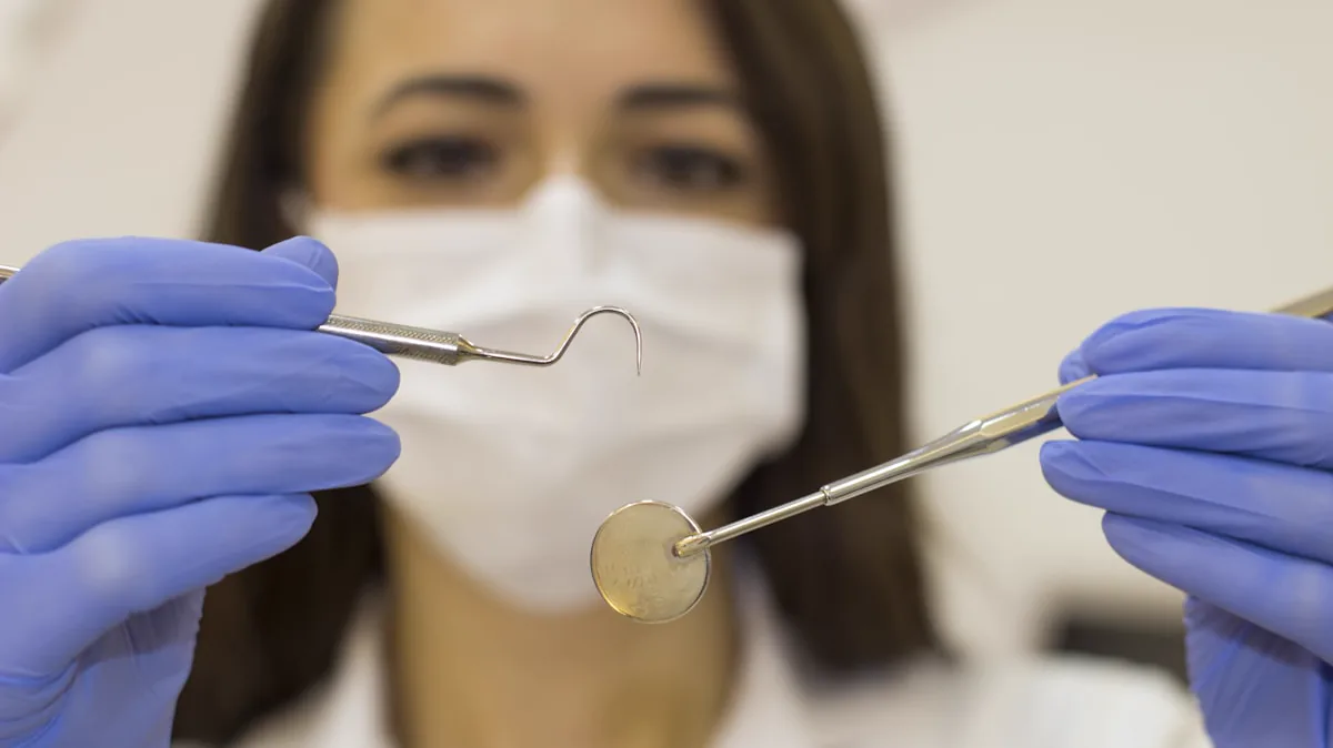 Dentist holding a dental mirror and probe during an oral examination