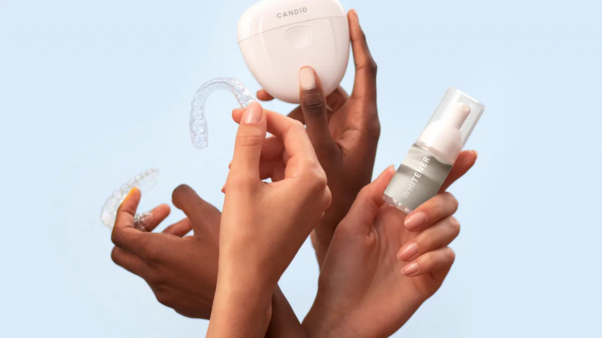 Hands holding clear dental trays, cases, and a whitening product