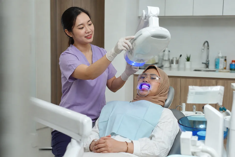 Dentist positioning a whitening light over a patient wearing protective eyewear in a dental chair